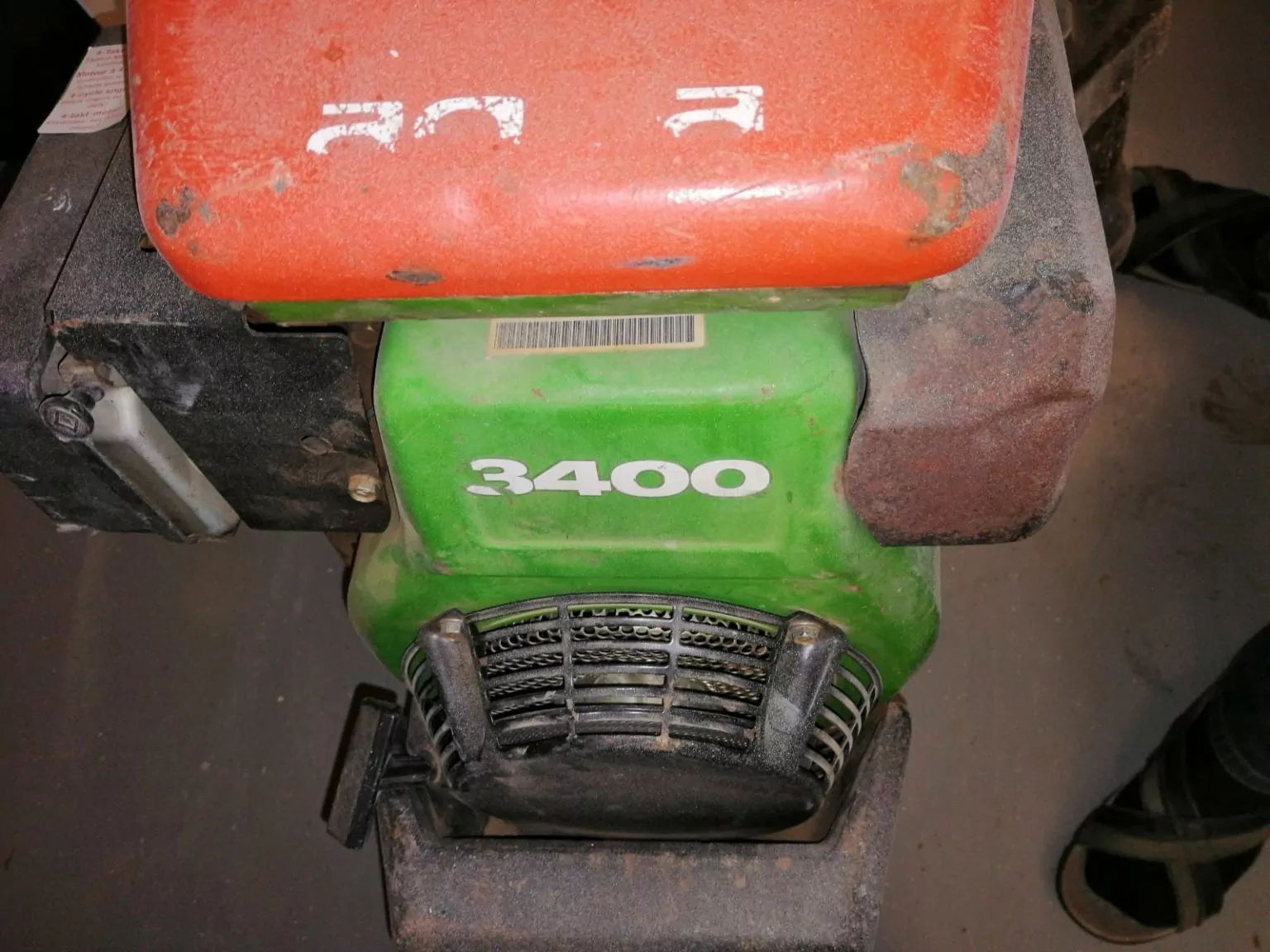 Eine Nahaufnahme eines grün-orangefarbenen Maschinenteils mit der Aufschrift „3400“. Der obere Teil ist orange, während der mittlere Teil grün mit weißem Text ist. Teile der Maschine weisen Abnutzungserscheinungen auf und an der Unterseite ist eine Entlüftung sichtbar.