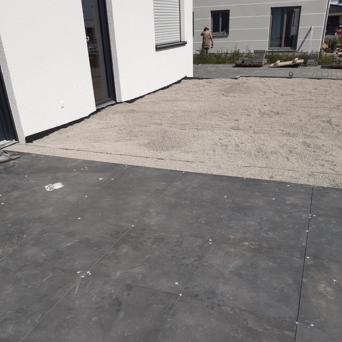 Terrasse im Umbau: frisch verlegte dunkle Steinfliesen und Kies