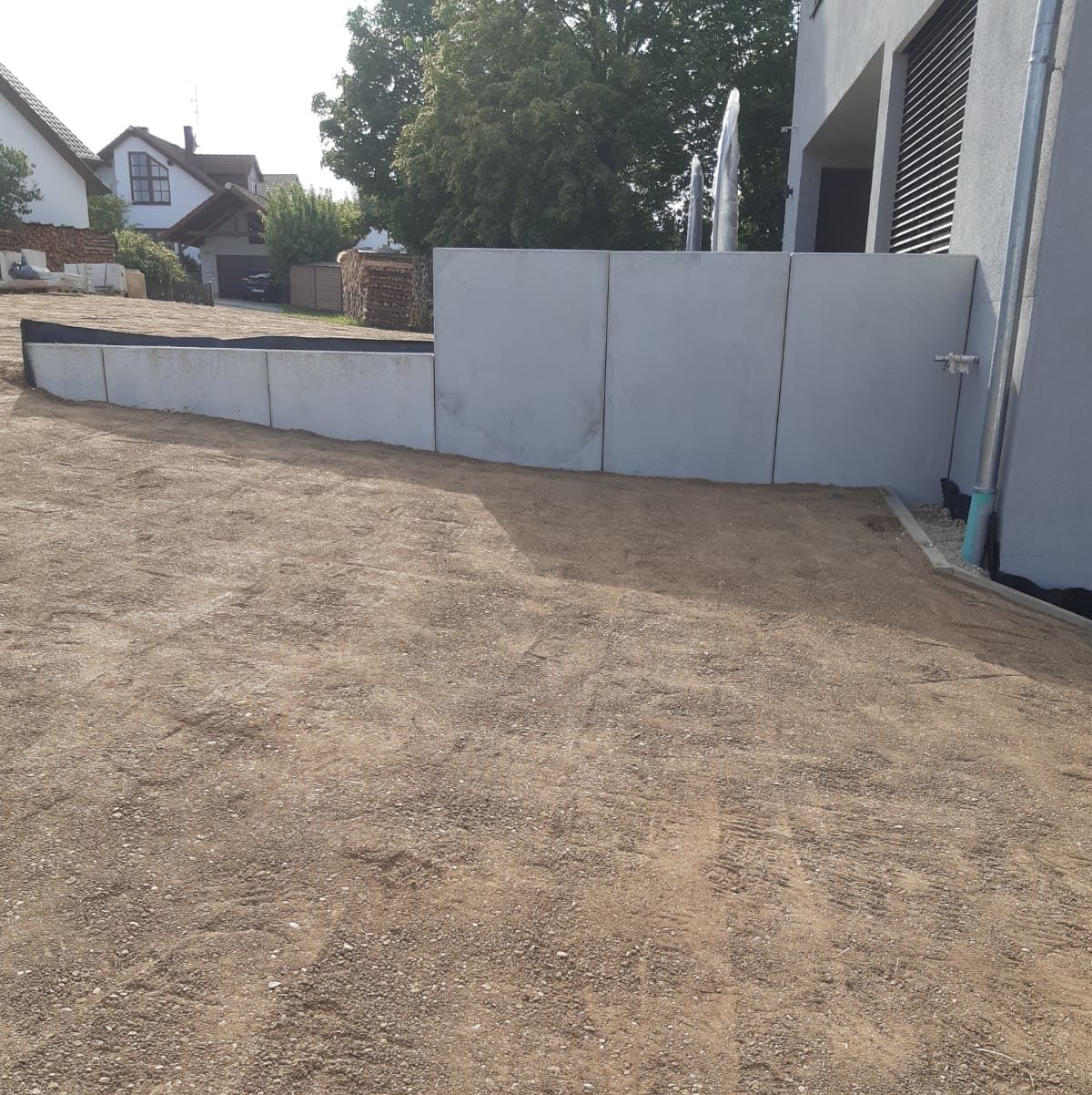 Kiesauffahrt zu einem hellgrauen Gebäude mit Betonmauer